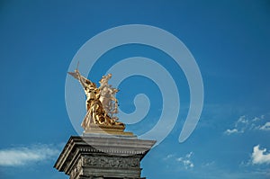 Marble column with golden statue adorning the Alexandre III bridge over the Seine River in Paris.